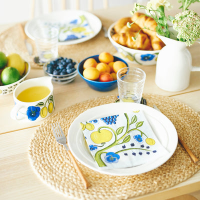 Table setting with decorative plates, cups, and a napkin featuring fruit and floral patterns.