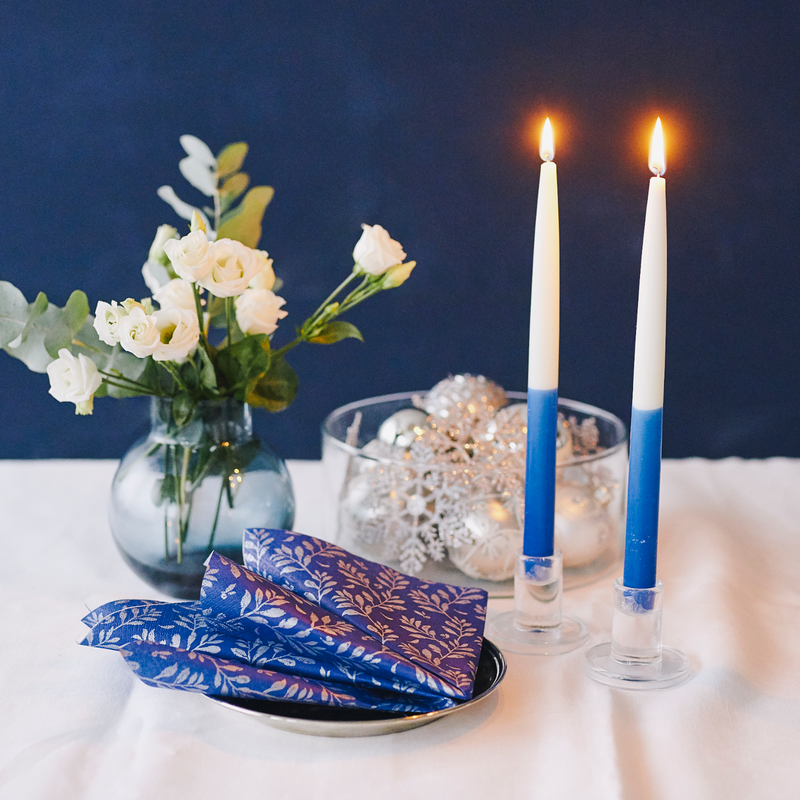 Decorative setup with candles, flowers, and gift wrap on a table against a dark blue background.