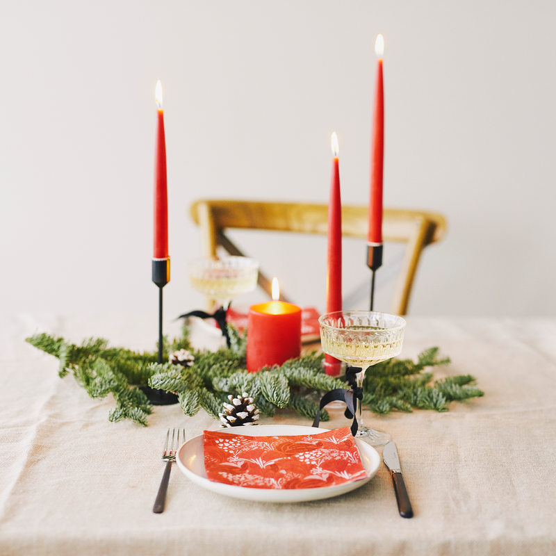 Table setting with red candles, greenery, and a plate of food on a white tablecloth.