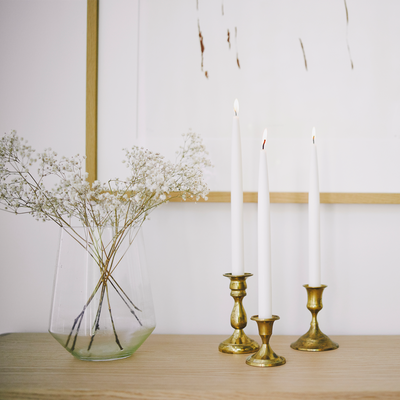 Decorative setup with a vase of dried flowers, candles, and brass candle holders on a wooden surface.