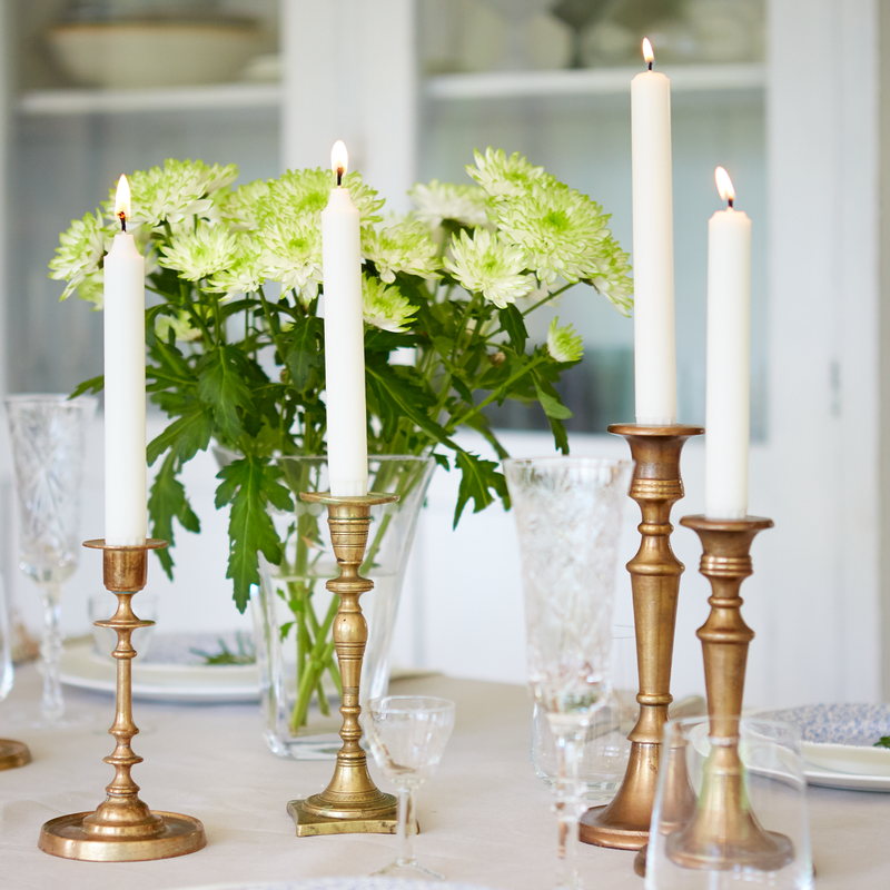 Decorative table setting with candles in brass candlesticks and a vase of green flowers.