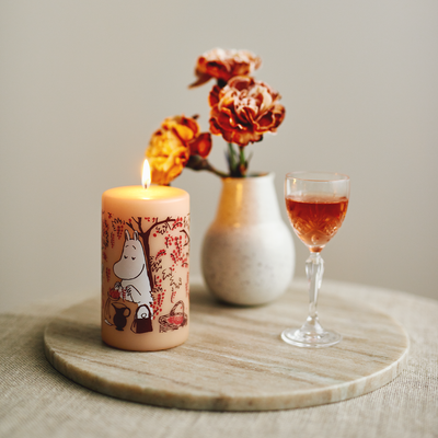 Candle with a design, wine glass, and vase with flowers on a wooden surface.
