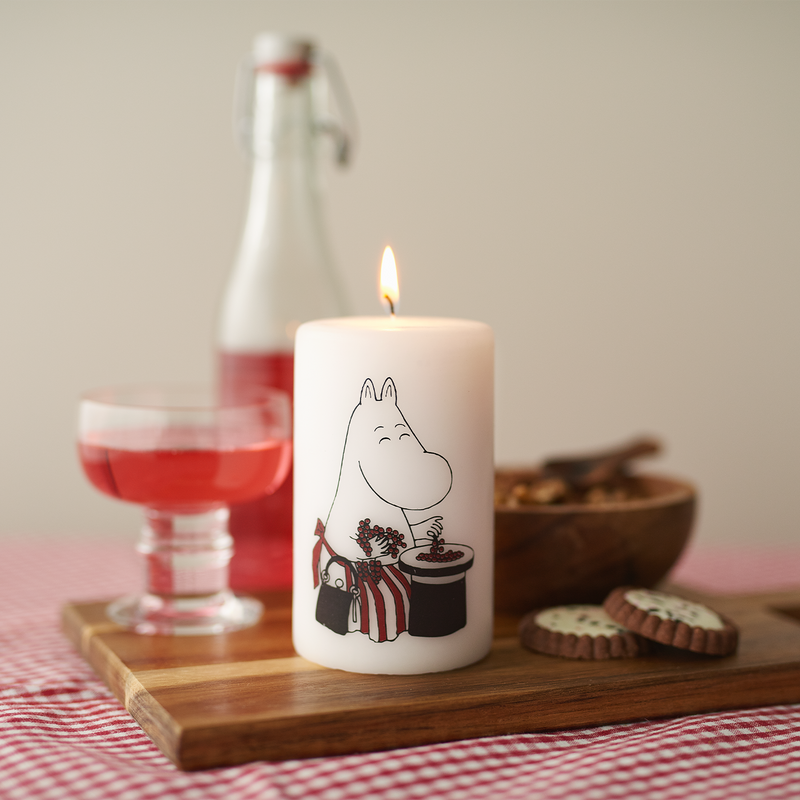 Candle with a character design on a wooden tray with a bottle, glass, and cookies in the background.