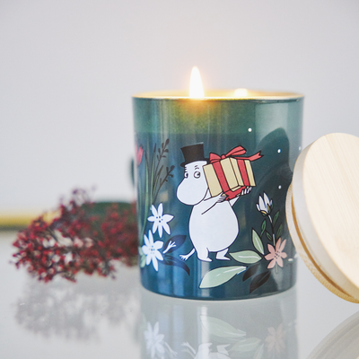 Candle in a decorative container with a character holding a gift, surrounded by flowers on a light background.