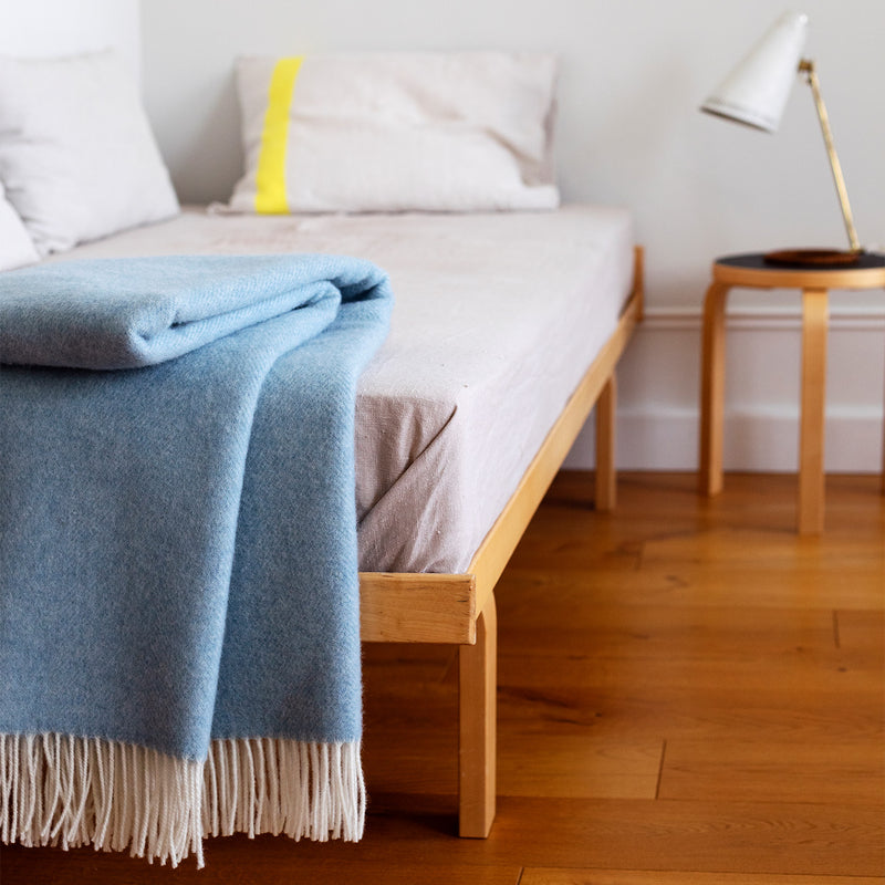 Bed with blue blanket and white pillows in a room with wooden floor and lamp.