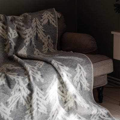Gray and white patterned blanket draped over a brown sofa against a dark wall.