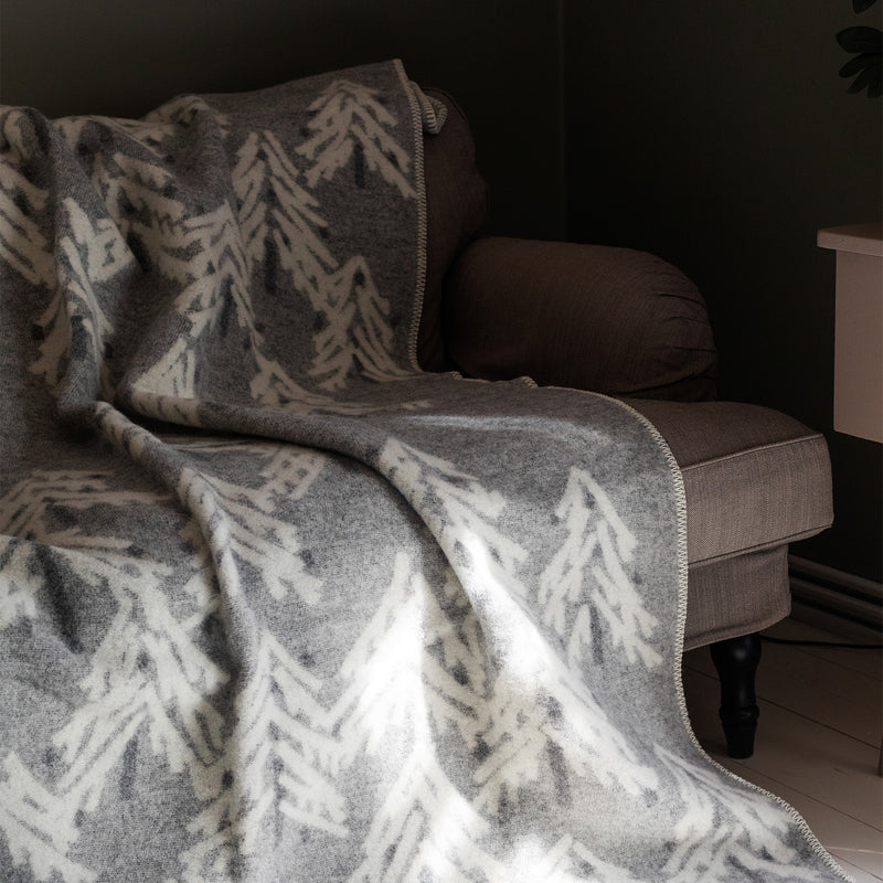 Gray and white patterned blanket draped over a brown sofa against a dark wall.