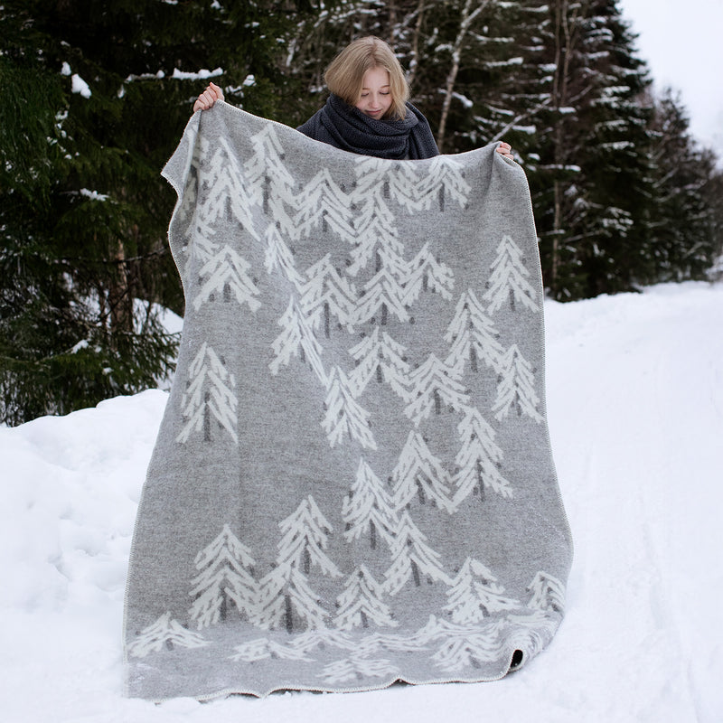 Person holding a gray and white patterned blanket in a snowy forest
