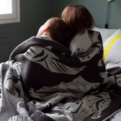 Two people wrapped in a patterned blanket on a bed.