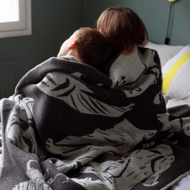 Two people wrapped in a patterned blanket on a bed.