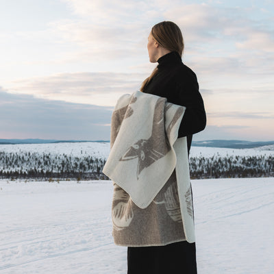 Person holding a patterned blanket in a snowy landscape