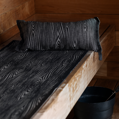 Black patterned pillow and mattress on a wooden bench in a wooden room.
