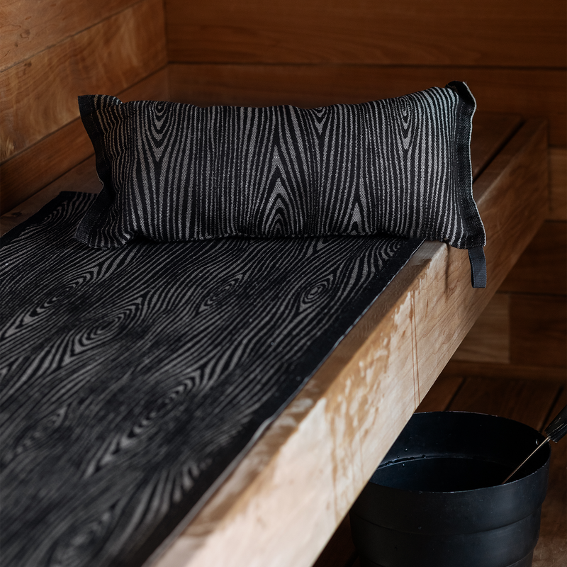 Black patterned pillow and mattress on a wooden bench in a wooden room.