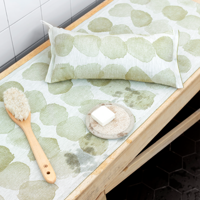 Green patterned mat with a wooden spoon and white block on a tiled floor.