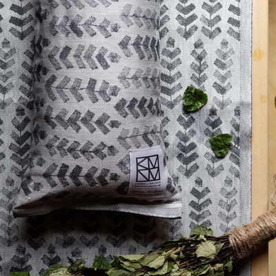 Textile with leaf pattern and brand label, accompanied by green leaves and a broom.