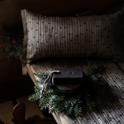Brown textured pillow on a wooden surface with a small bag and greenery.