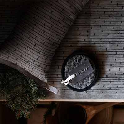 Round black leather item with a tag on a textured surface, surrounded by greenery.