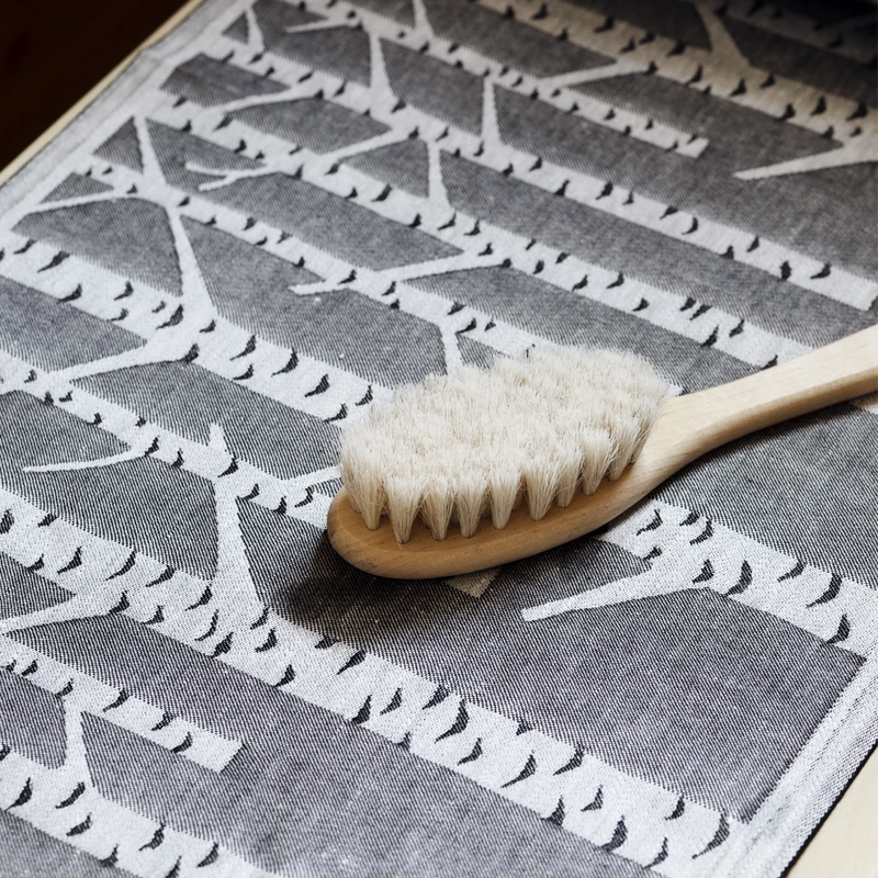 Wooden brush with white bristles on a gray and white patterned fabric background
