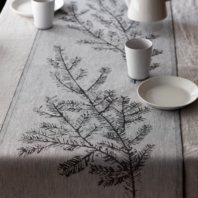 Table setting with a decorative tablecloth featuring black tree branches on a wooden table.