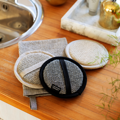 Three exfoliating pads on a wooden surface with a sink in the background