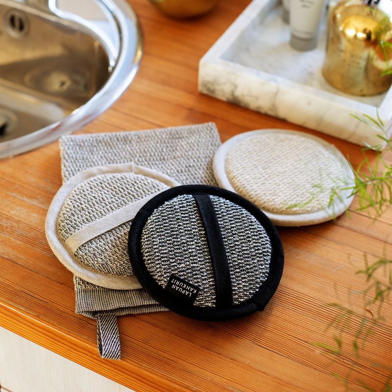 Three exfoliating pads on a wooden surface with a sink in the background