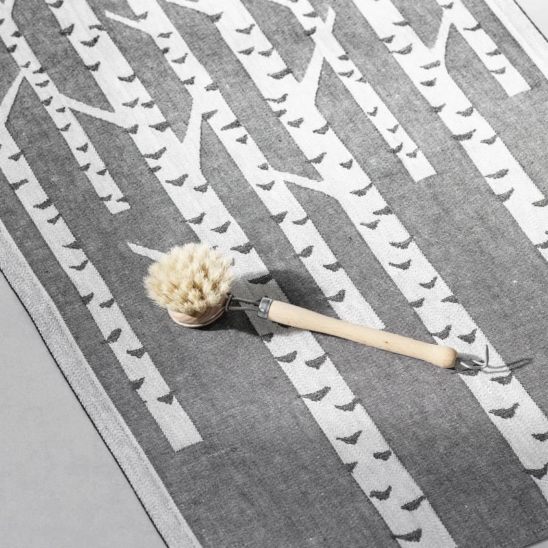 Cleaning brush with a natural bristle head on a gray and white patterned mat.