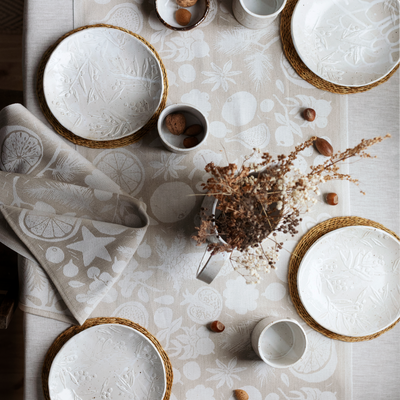 Table setting with white ceramic plates, bowls, and cups on a patterned tablecloth.