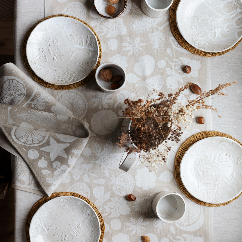 Table setting with white ceramic plates, bowls, and cups on a patterned tablecloth.