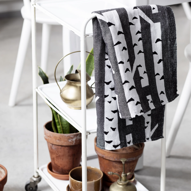 Black and white patterned towel draped over a white metal cart with potted plants and decorative items.