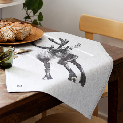Dining table with a towel featuring a deer design, bread, and a glass.
