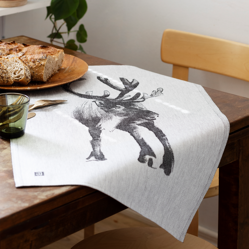 Dining table with a towel featuring a deer design, bread, and a glass.