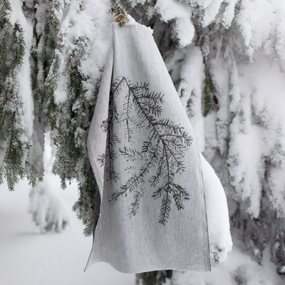 White towel with black tree branch design hanging on a snow-covered branch