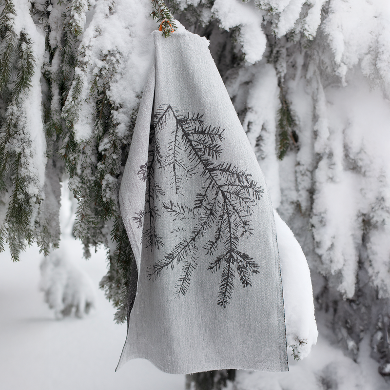 White towel with black tree branch design hanging on a snow-covered branch