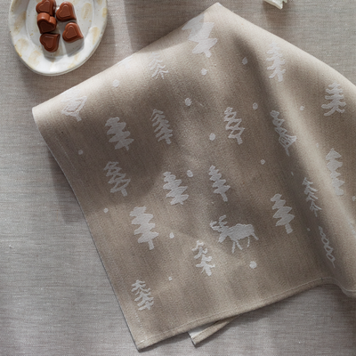 Folded beige towel with white tree and moose pattern on a textured surface.