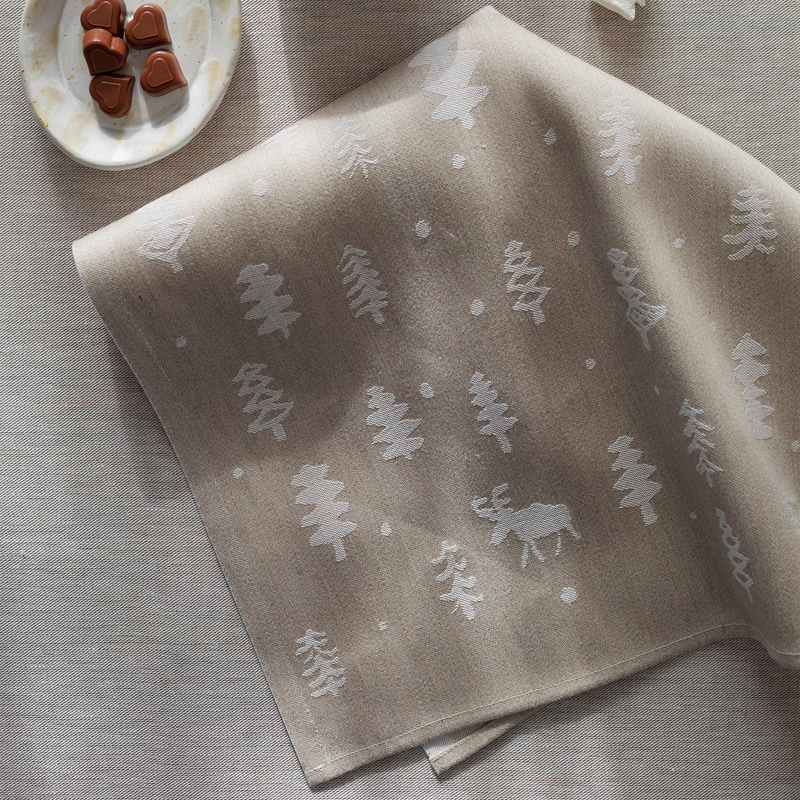 Folded beige towel with white tree and moose pattern on a textured surface.