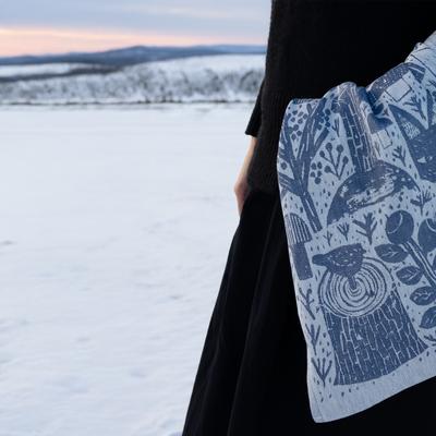 Person wearing a black coat with a blue patterned scarf against a snowy landscape.