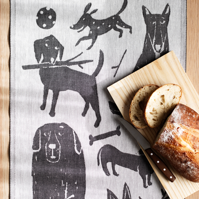 Tea towel with dog illustrations next to a wooden board with bread