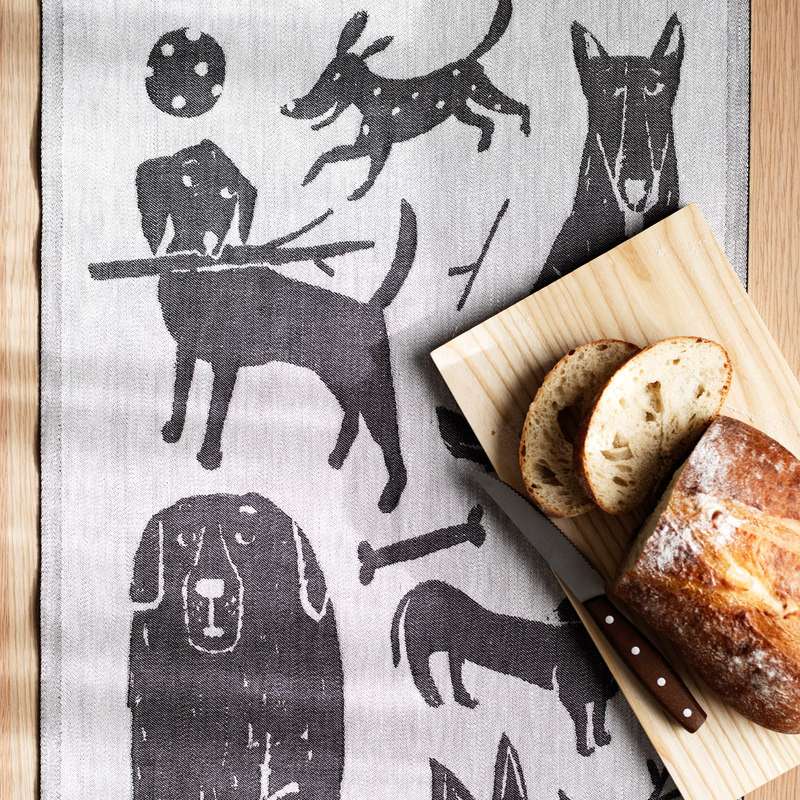 Tea towel with dog illustrations next to a wooden board with bread