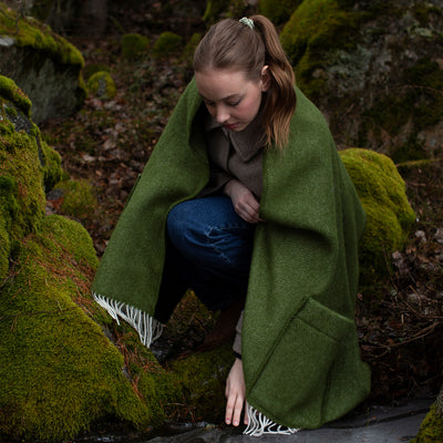 Woman wrapped in a green blanket sitting on a mossy rock in a forest