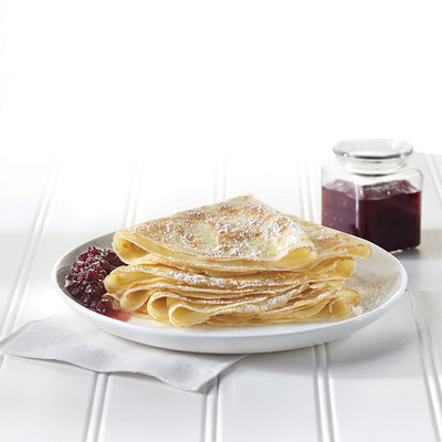 Stack of swedish pancakes on a plate with a jar of jam on a white background