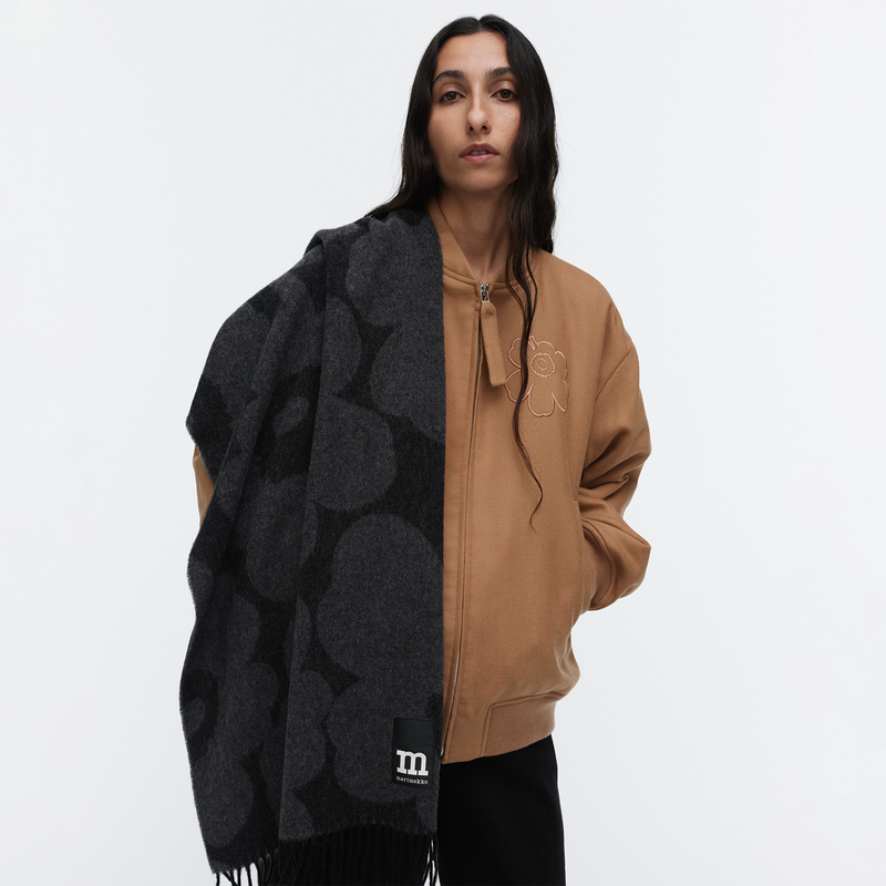 Person wearing a black and gray scarf and tan jacket on a white background