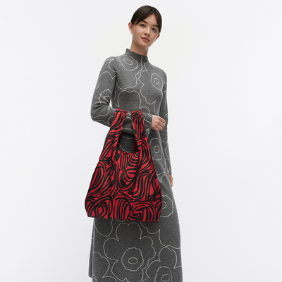 Woman holding a red and black patterned bag against a white background