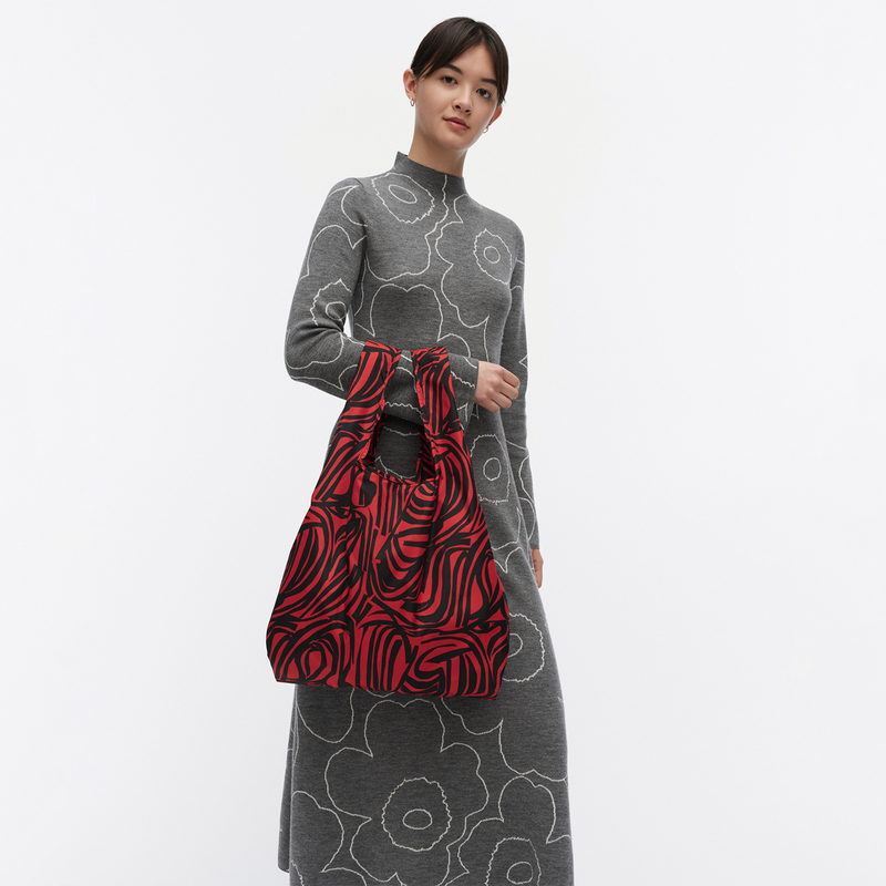 Woman holding a red and black patterned bag against a white background