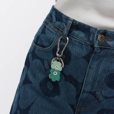 Blue denim skirt with a floral keychain on a plain background
