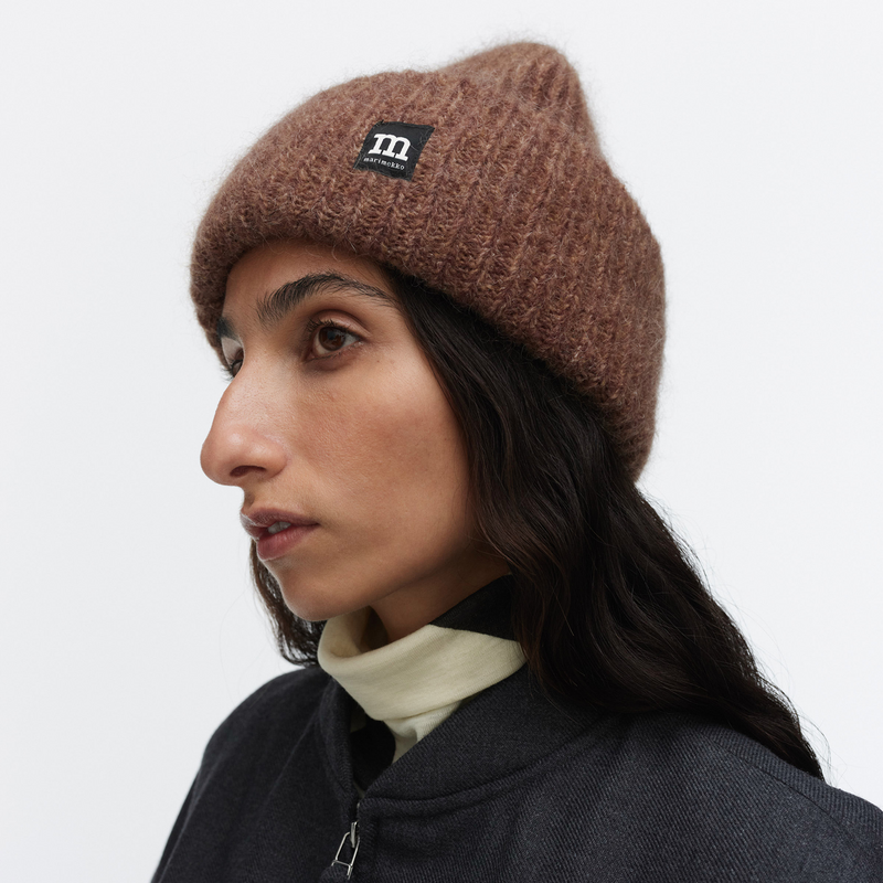 Person wearing a brown knit beanie with a logo on a white background
