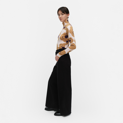 Person wearing a patterned top and black pants on a white background