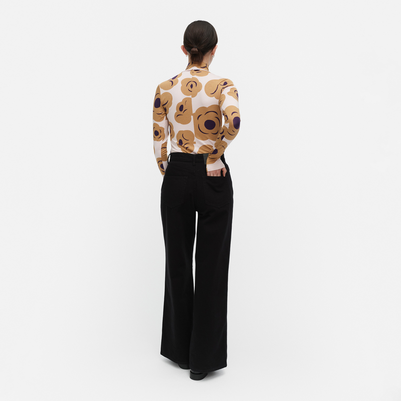 Person wearing a patterned top and black pants on a white background