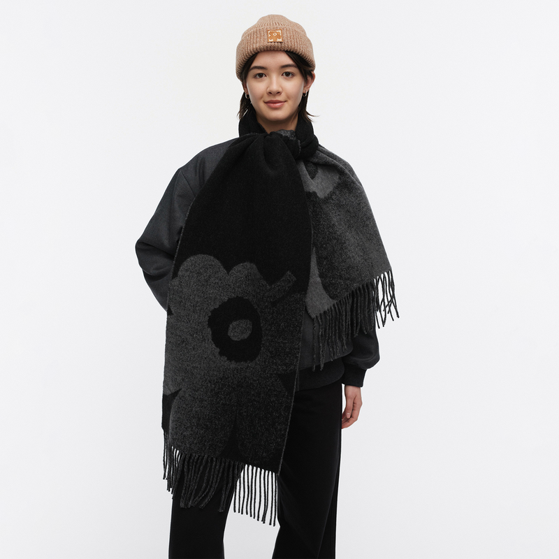 Person wearing a black and gray patterned poncho with fringes on a white background