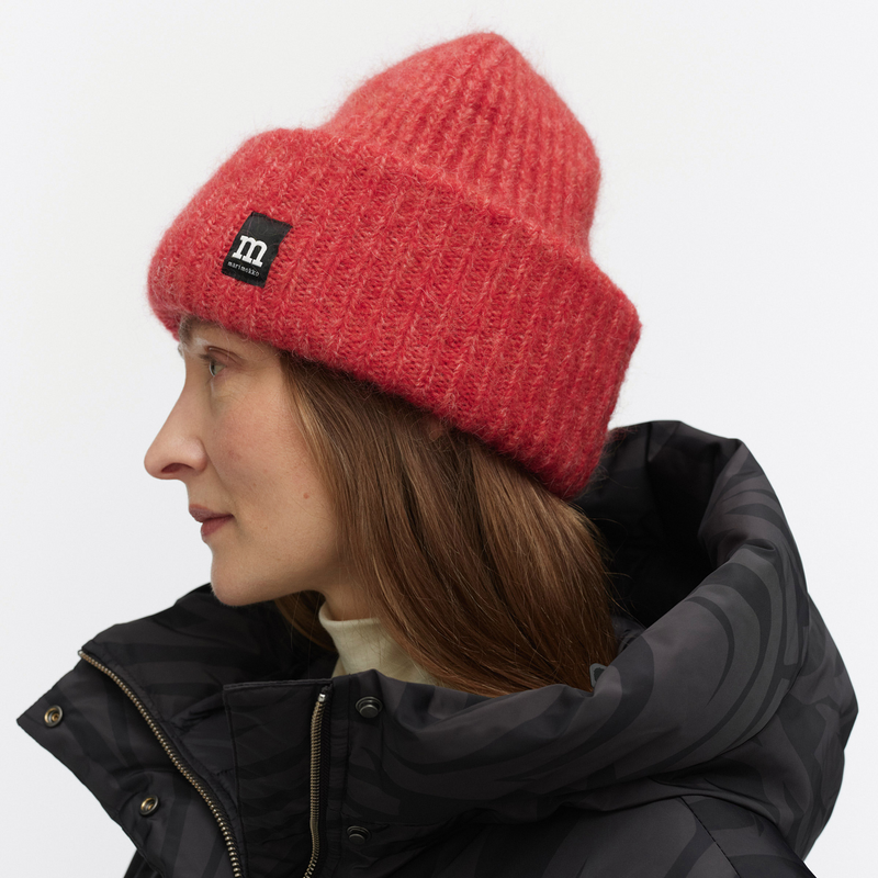 Person wearing a red knit beanie with a brand logo on a white background