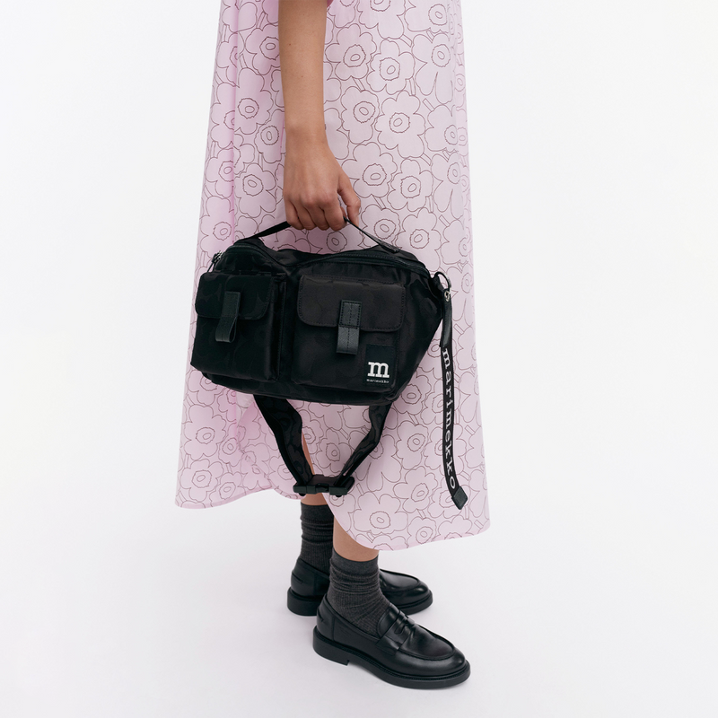 Person holding a black bag with a visible brand logo on a white background